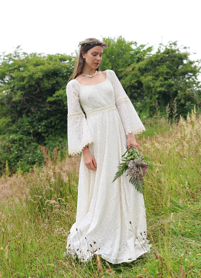 Irish Celtic bridal gown in a meadow, Bébhinn Boho Lace Wedding Dress in sustainable cotton lace with bell sleeves and bouquet.