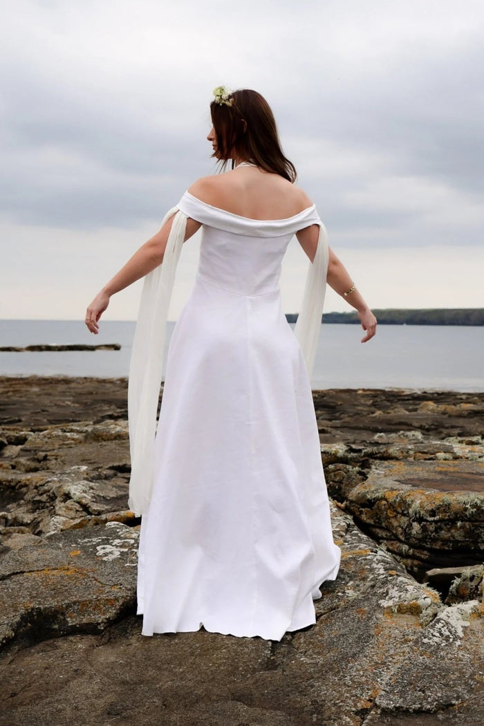 Back view of minimalist ivory boho bridal gown with off shoulder neckline and long floating sleeves