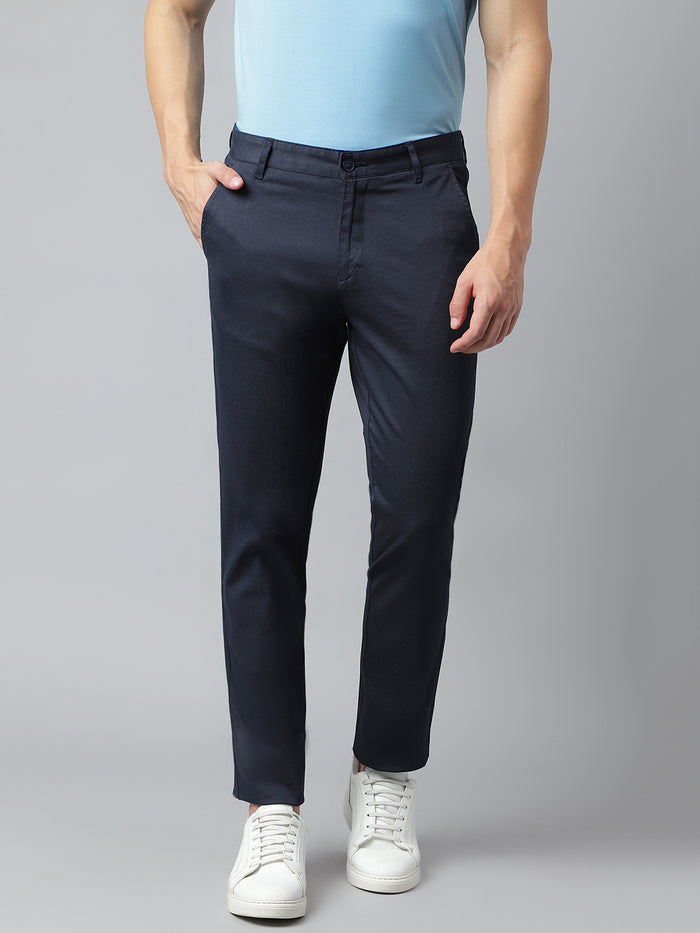 A man wearing navy slim fit mid-rise casual trousers and a light blue shirt with white shoes.