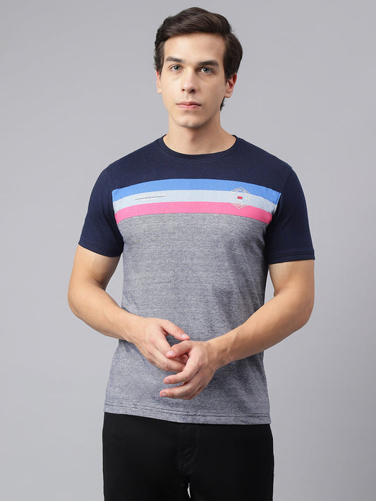 A man wearing a grey crew neck T-shirt with color blocks in navy and pink on the chest area, paired with black trousers.