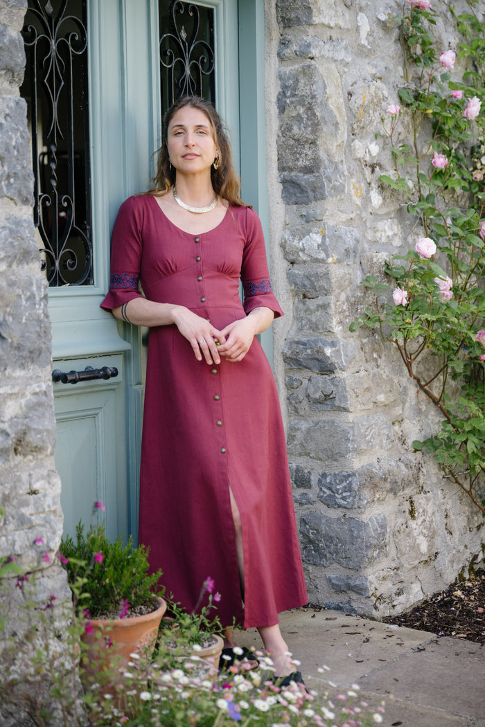 Burgundy Celtic maxi dress with button front and front slit styled beside a stone doorway