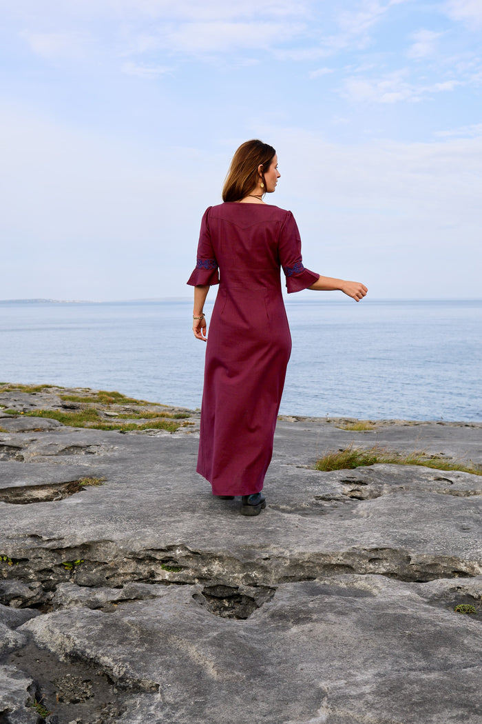 Back view of burgundy Celtic maxi dress with fitted waist and Celtic embroidered flared sleeves by the sea