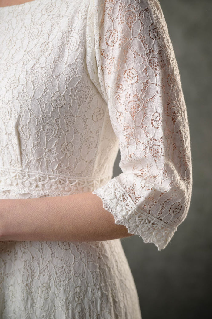 Close-up of natural cotton ivory lace bridal dress showing floral lace sleeve, scalloped cuff and delicate waist trim